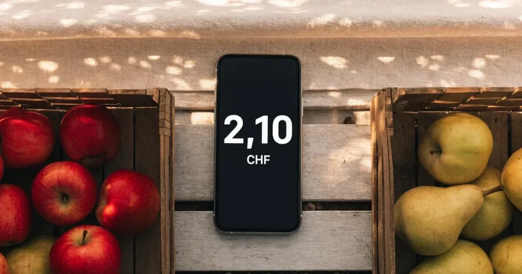 Ein Smartphone mit dunklem Display liegt auf dem Holztisch eines Marktstands zwischen Äpfeln und Birnen, morgendliches Licht fällt durch eine Plane.